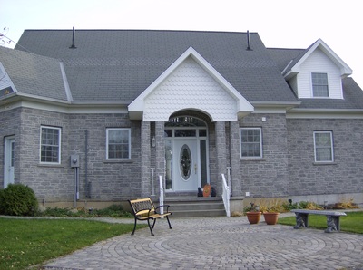 The front of a grey stone home with a stone patio and walkway.